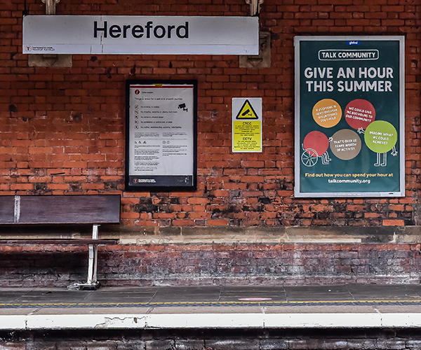 Talk Community poster on a railway platform - part of the 'Give an hour this summer' campaign