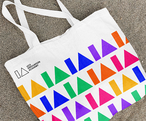 A tote bag featuring the Innovation Academy logo in a colourful repeat pattern